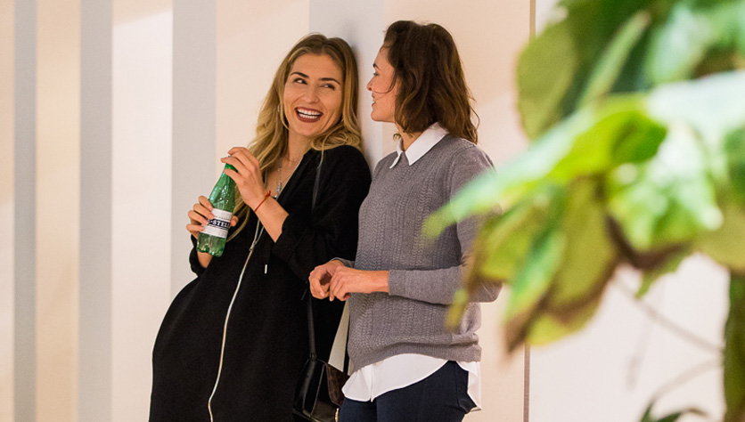 Two women doing dry January and talking while leaning against wall one is holding a water bottle