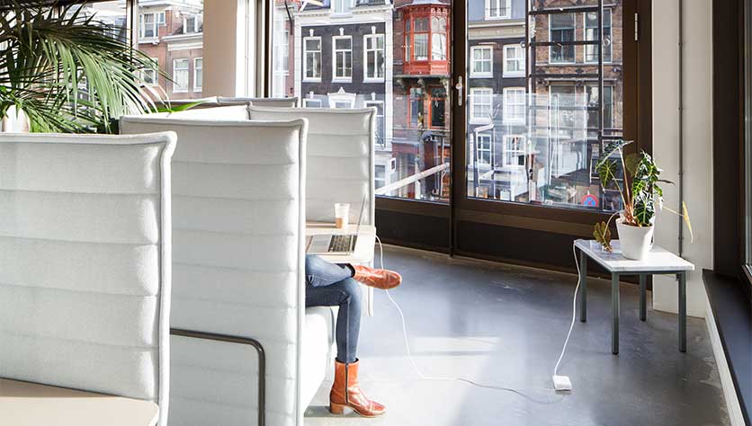 Woman sitting in lounge chair at spaces vijzelstraat with view on canal houses