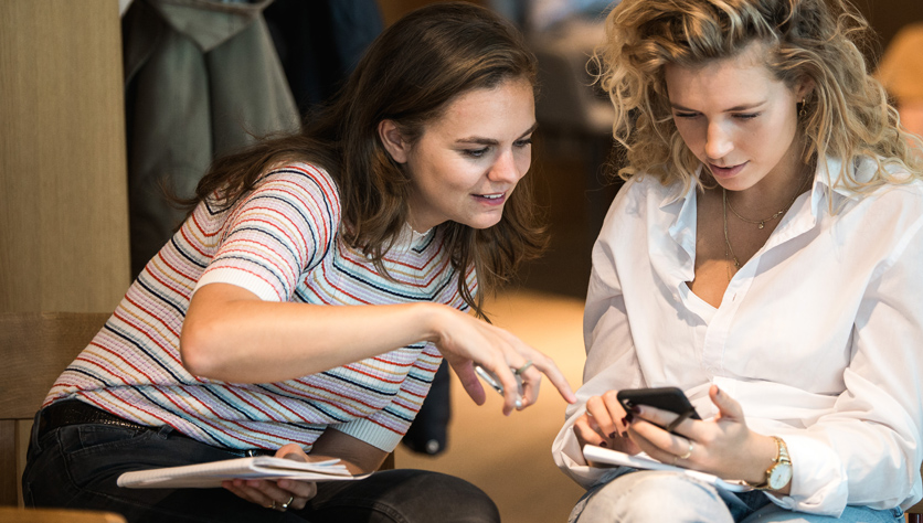 two women in meeting room looking at phone and smiling